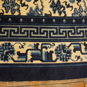 Navy and cream rug border featuring Greek key and floral motifs rests on worn wooden flooring.