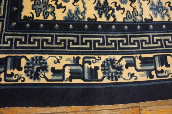 Navy and cream rug border featuring greek key and floral motifs rests on worn wooden flooring.