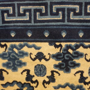Detailed view of a rug showing a blue fret border above a cream field with navy cloud motifs.