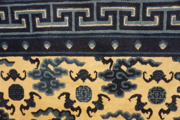Detailed view of a rug showing a blue fret border above a cream field with navy cloud motifs.