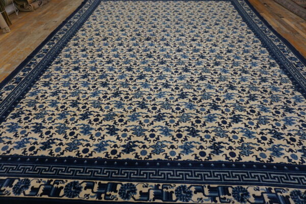 Cream and blue rug featuring a repeating cloud pattern and geometric borders on wood flooring.