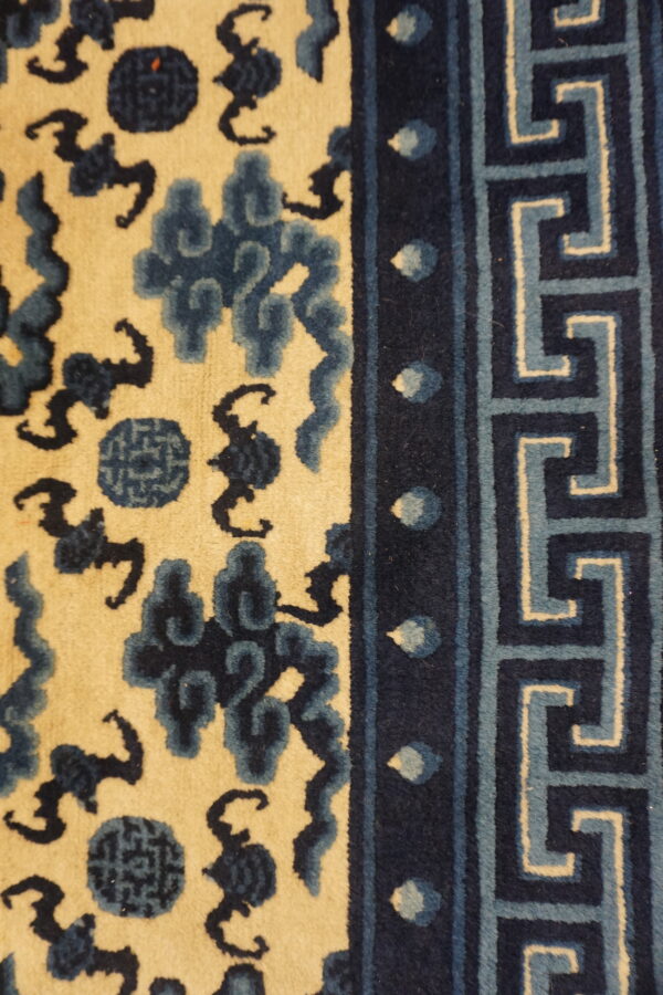 Creamy tan rug field featuring dark blue cloud motifs and a navy blue greek key border.