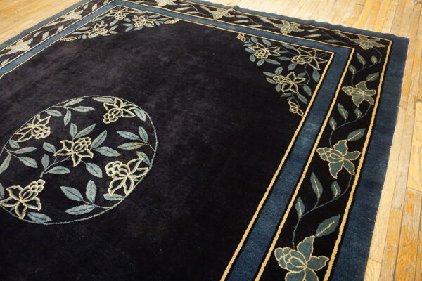 Dark navy rug featuring a floral medallion and borders in teal and gold against distressed wood planks.
