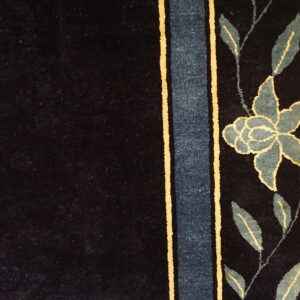 Dark navy rug detail showing a border of teal leaves, a flower, and vertical blue and gold stripes.