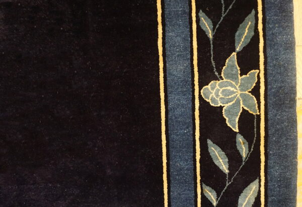 Dark navy rug detail showing a border of teal leaves, a flower, and vertical blue and gold stripes.