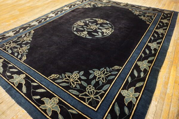 Dark blue high-pile rug with a floral medallion and borders in light blue and yellow on wood flooring.
