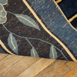 Close-up of a dark blue floral rug rolled back, showing the woven underside on distressed wood flooring.