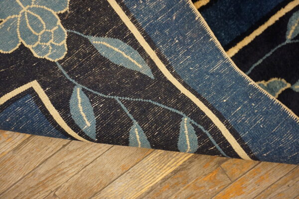 Close-up of a dark blue floral rug rolled back, showing the woven underside on distressed wood flooring.