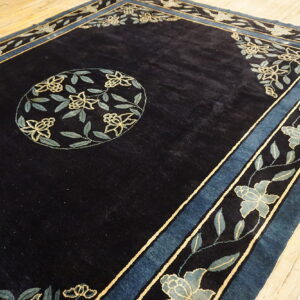 Navy blue rug with a light blue floral border and center medallion rests on pale wood flooring.