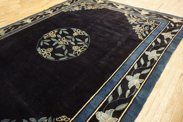 Navy blue rug with a light blue floral border and center medallion rests on pale wood flooring.