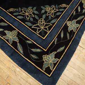 Dark blue rug corner showing gold-outlined teal floral motifs on worn light hardwood planks.