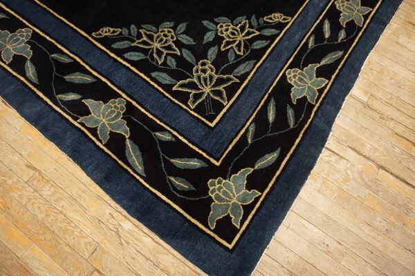 Dark blue rug corner showing gold-outlined teal floral motifs on worn light hardwood planks.