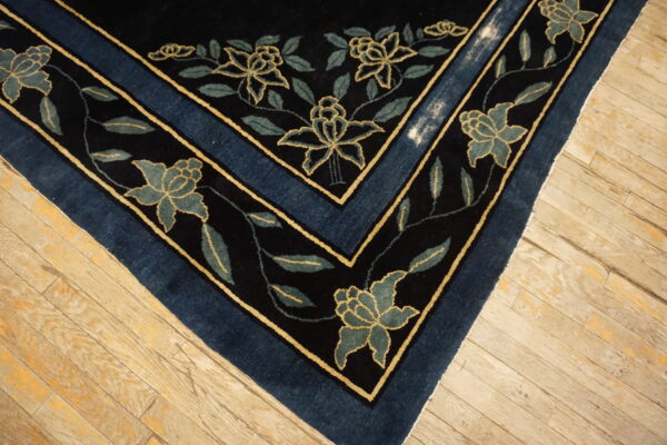 A dark blue rug featuring a seafoam floral pattern and gold outlines, lying on distressed wood flooring.