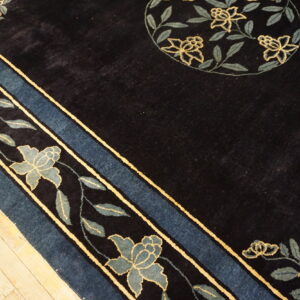 Plush dark rug with a slate blue and yellow floral border rests on light plank wood flooring.