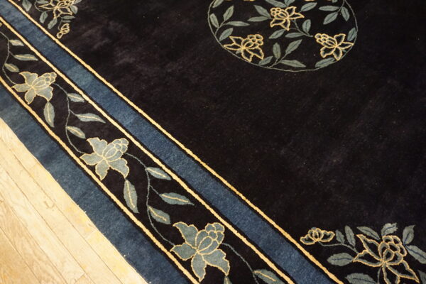 Plush dark rug with a slate blue and yellow floral border rests on light plank wood flooring.
