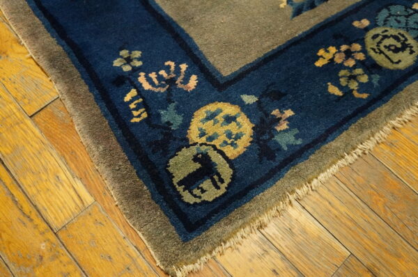 High-pile rug corner showing blue border with floral and animal motifs on yellow wood floor.