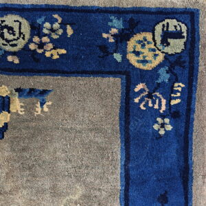 Muted gray rug field bordered by a dense royal blue edge with yellow and pale blue floral patterns.