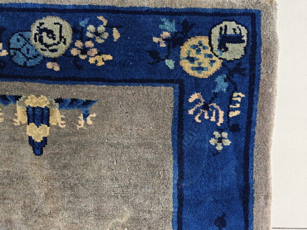 Muted gray rug field bordered by a dense royal blue edge with yellow and pale blue floral patterns.