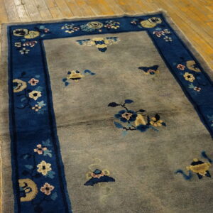 A gray field rug featuring a wide blue floral border rests on rustic yellow wooden plank flooring.