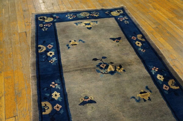 A gray field rug featuring a wide blue floral border rests on rustic yellow wooden plank flooring.