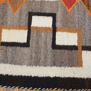 Textured gray, white, and black geometric rug with orange and brown accents rests on wood flooring.
