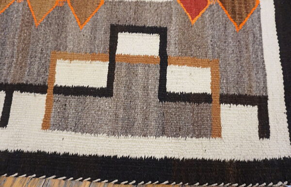 Textured gray, white, and black geometric rug with orange and brown accents rests on wood flooring.