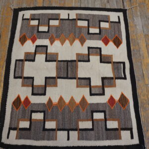 Flatweave rug with white, gray, black, brown, and orange geometric patterns on distressed wood floor.