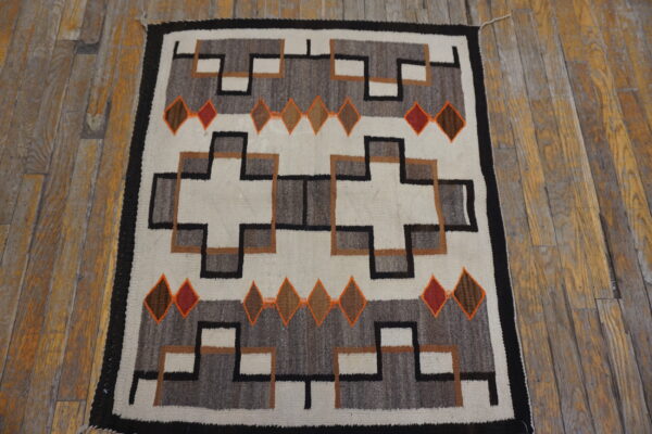 Flatweave rug with white, gray, black, brown, and orange geometric patterns on distressed wood floor.
