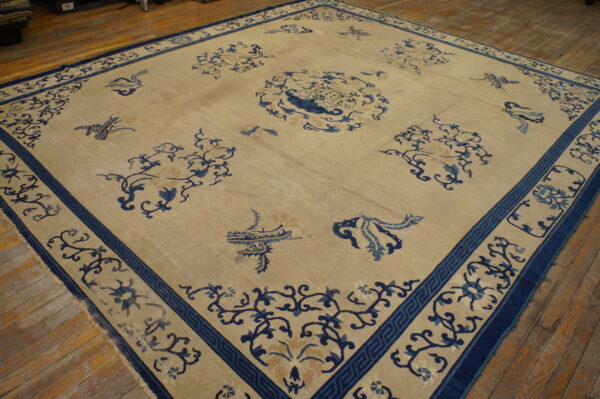 Light beige area rug with a scattered deep blue motif and detailed border on rustic hardwood flooring.