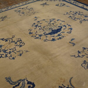 Beige rug with dark blue vine motifs and a thick border sits on rustic wood planks.