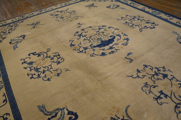 Beige rug with dark blue vine motifs and a thick border sits on rustic wood planks.