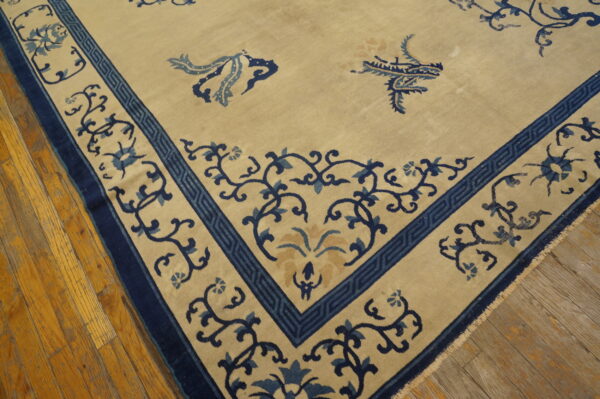Beige rug featuring detailed indigo and light blue borders with scrolling motifs on distressed hardwood flooring.
