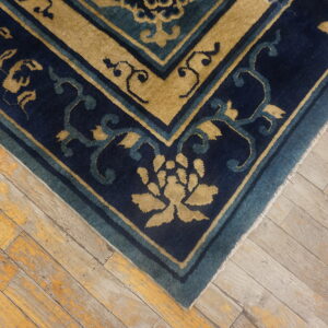 A navy blue and tan rug border with a floral pattern rests on rustic distressed wood flooring.