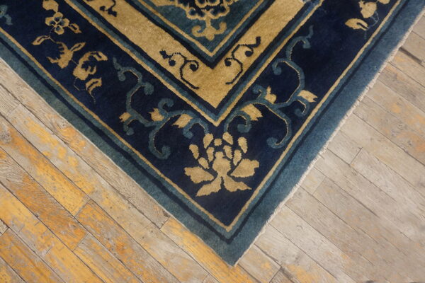 A navy blue and tan rug border with a floral pattern rests on rustic distressed wood flooring.