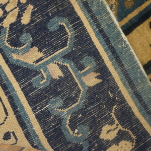 A detailed view of a navy, light blue, and tan geometric patterned weave folded over a high-pile rug.