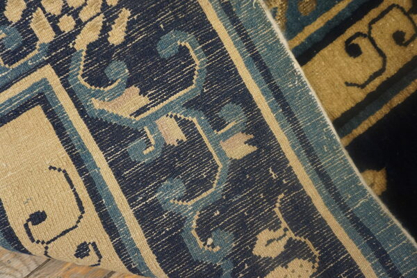 A detailed view of a navy, light blue, and tan geometric patterned weave folded over a high-pile rug.