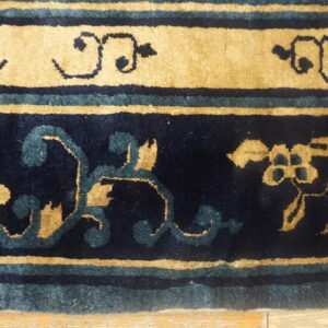 Detailed view of a navy and tan rug border with teal stripes and stylized floral motifs on a wood floor.