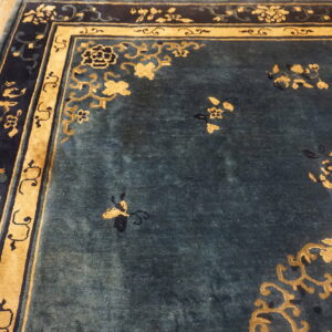 Teal and gold rug featuring a dense floral pattern and elaborate navy border on hardwood floors.