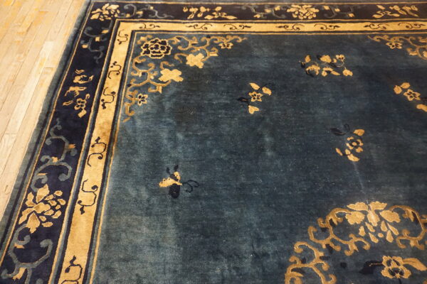 Teal and gold rug featuring a dense floral pattern and elaborate navy border on hardwood floors.