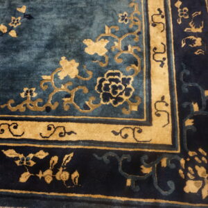 Detailed view of a blue and gold rug corner with floral designs resting on wood planks.