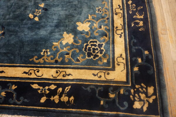 Detailed view of a blue and gold rug corner with floral designs resting on wood planks.