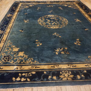 Teal floral rug with a golden medallion and multi-layered navy border on wooden floorboards.
