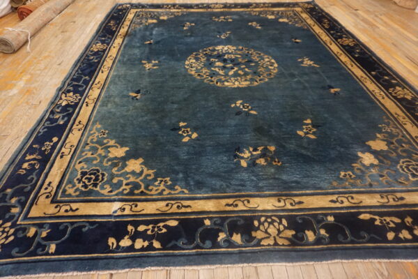 Teal floral rug with a golden medallion and multi-layered navy border on wooden floorboards.