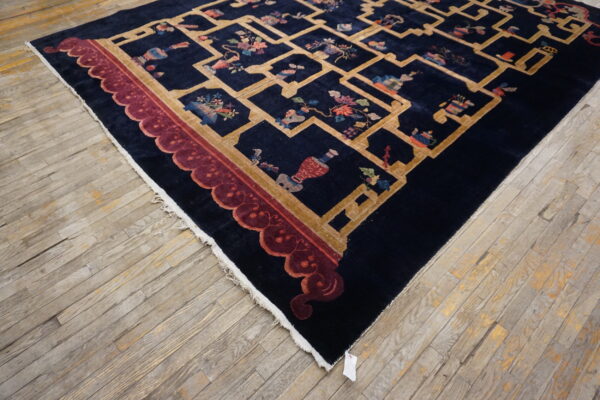 Navy rug with a gold trellis pattern, multicolored object motifs, and a maroon scalloped border on wood flooring.