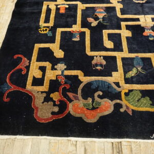 Close-up of a dark blue rug with gold geometric grid and colorful scrollwork on plank flooring.