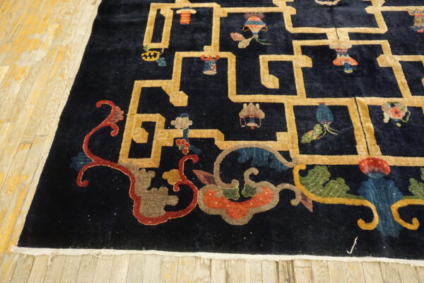 Close-up of a dark blue rug with gold geometric grid and colorful scrollwork on plank flooring.