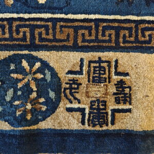 Coarse pile rug detail in dark blue and tan with a meander border and central symbols.