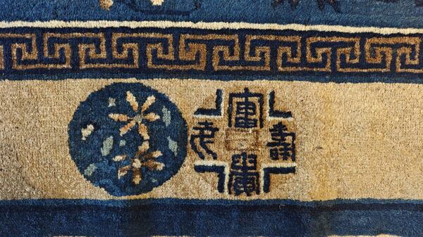 Coarse pile rug detail in dark blue and tan with a meander border and central symbols.