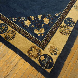 Deep blue rug with gold floral patterns and a wide tan border resting on distressed wood flooring.