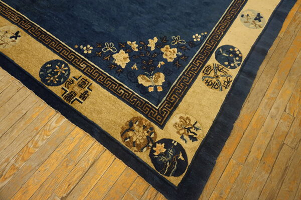 Deep blue rug with gold floral patterns and a wide tan border resting on distressed wood flooring.